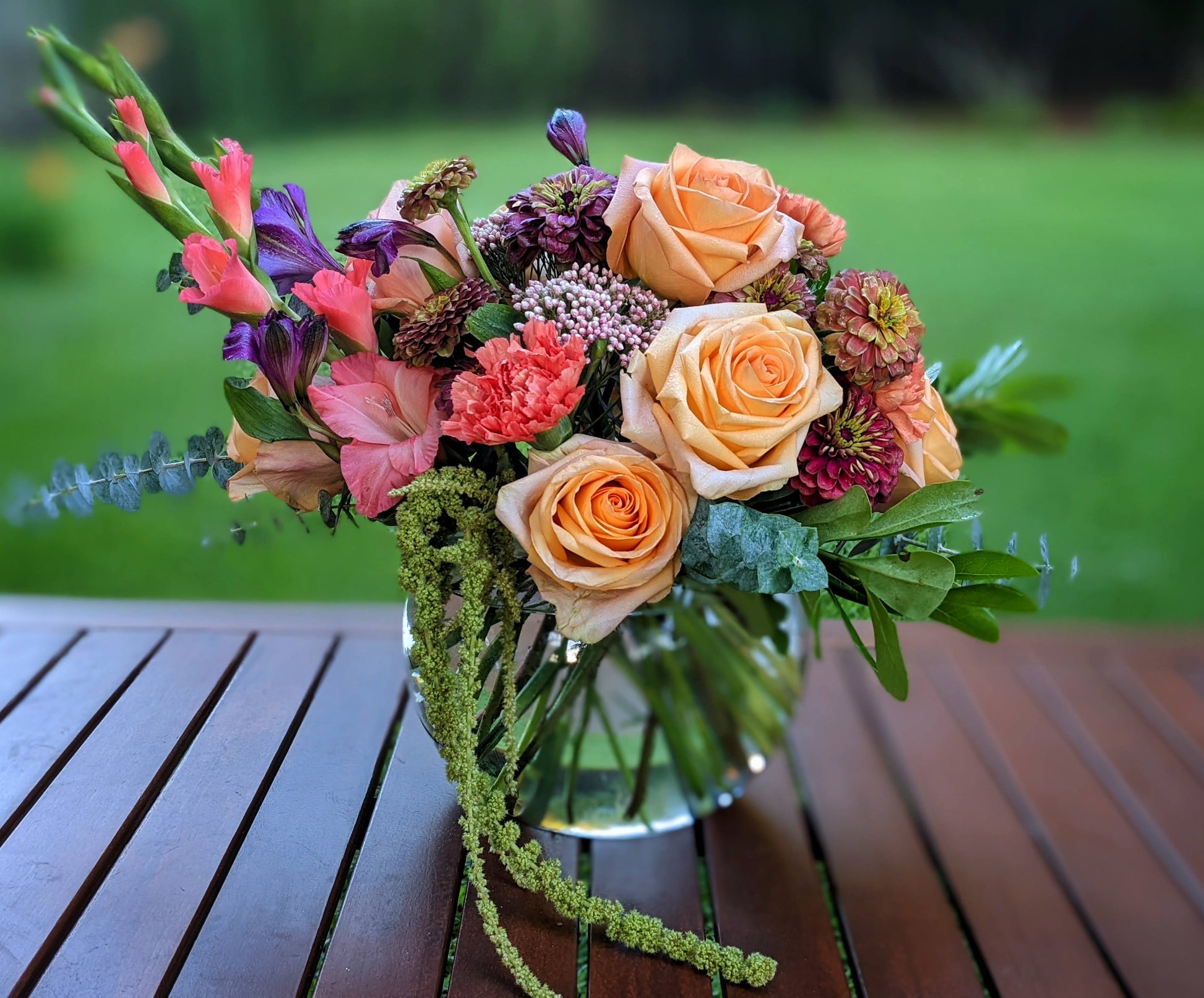 Bouquet of flowers in a vase on a wooden surface with a blurred green background